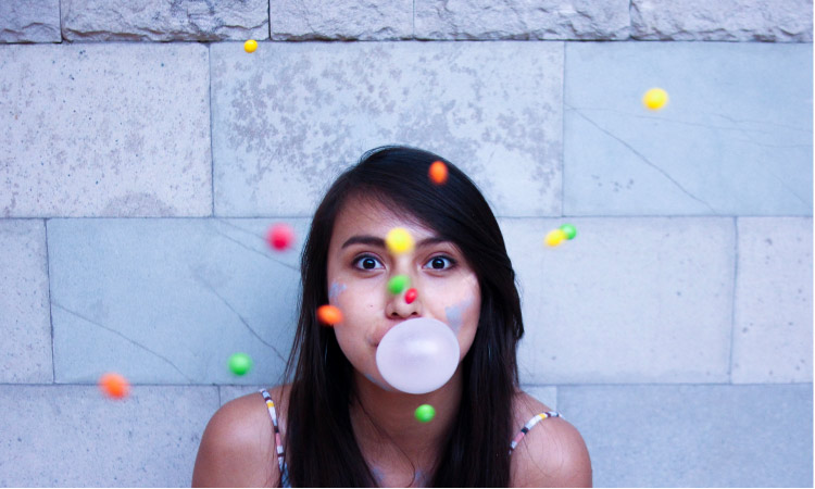 girl blowing a gum bubble with colored balls floating around her head